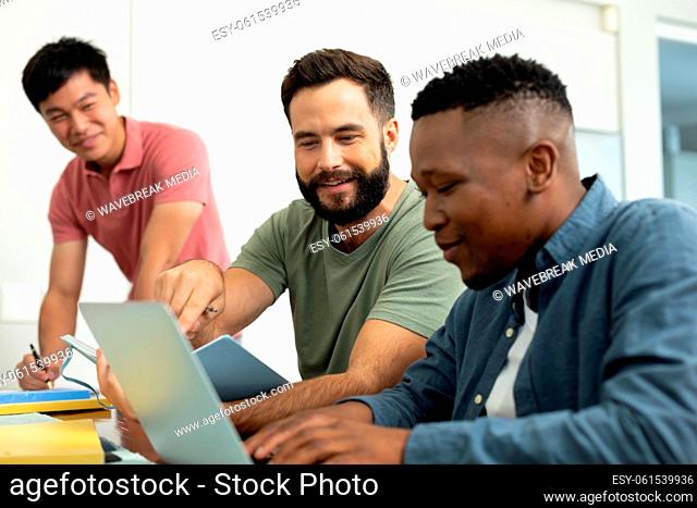 Smiling multiracial male coworkers looking at businessman working over laptop in office