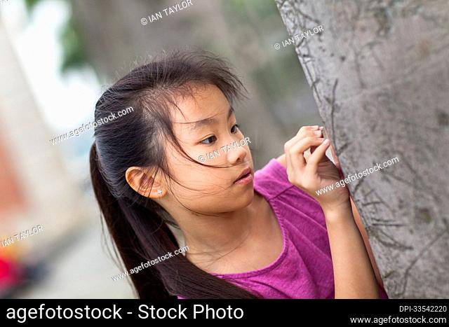 Outdoor portrait of a girl looking at the detail of tree bark; Hong Kong, China