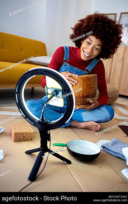 Afro woman with basket live streaming through smart phone in living room