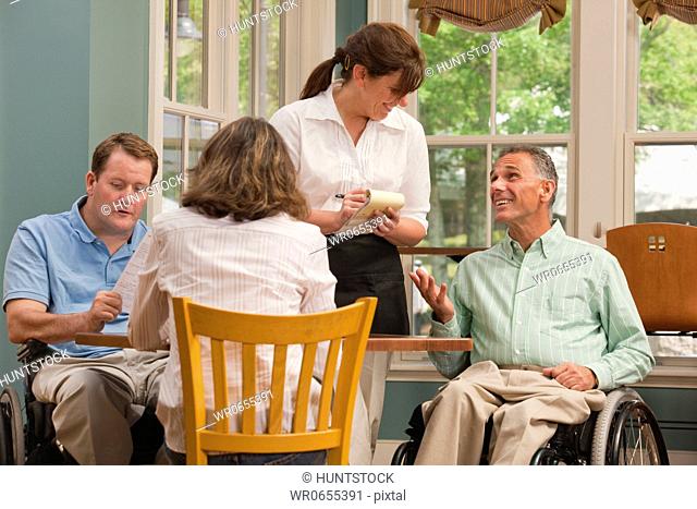 Two men in wheelchairs and a friend ordering food in a cafe