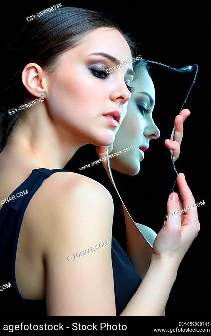 Girl with a shard of the mirror. Female with mirror shard in hand posing on gray background. Face reflection in mirror splinter