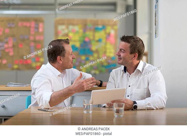 Two businessmen with tablet talking in office