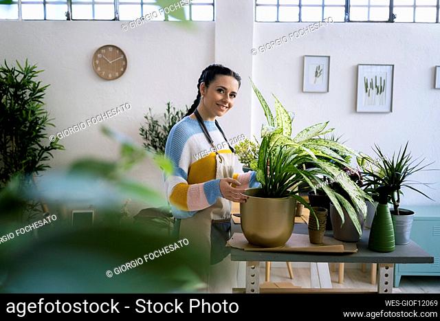 Smiling young woman standing by plant at table at workshop