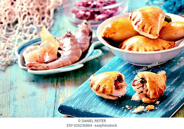 Close Up of Baked Seafood Empanada Pastries Served on Blue Cutting Board and Surrounded by Fresh Ingredients on Nautical Themed Blue Painted Table with Fishing...