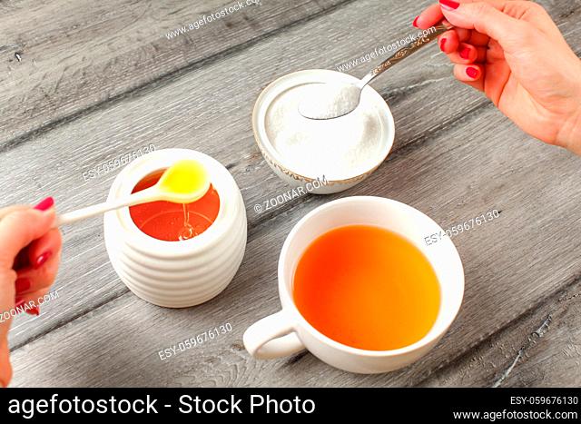 Young woman hands with red nails, holding spoon full of sugar and honey in other hand deciding what to put in her tea. Sugar vs honey concept