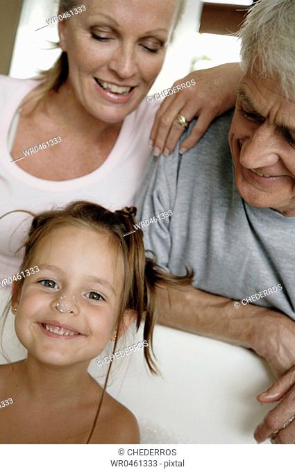 Portrait of a girl in a bathtub with her grandparents smiling behind her