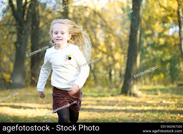 Beautiful little blonde girl runs in an autumn park. A child on a walk in the fall