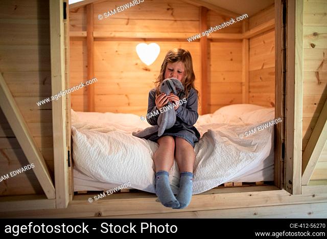 Linda chica jugando con conejito de peluche en la cama en el desván de madera