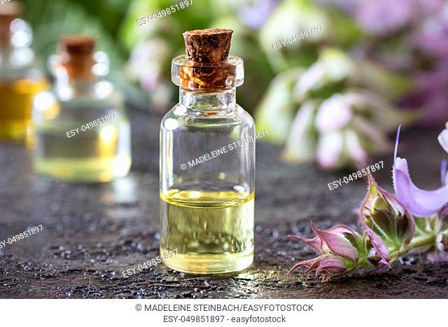 A bottle of essential oil with blooming clary sage twigs on a dark background