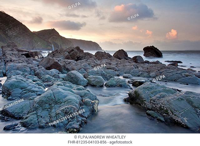 Stream flowing through rocks on beach at sunset, Mouthmill Beach, Windbury Point, North Devon, England, January
