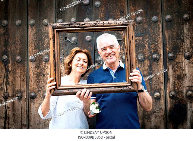 Portrait of senior couple, holding wooden frame in front of their faces, Mexico City, Mexico