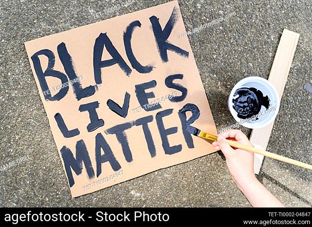 Woman's hand painting Black Lives Matter sign on cardboard
