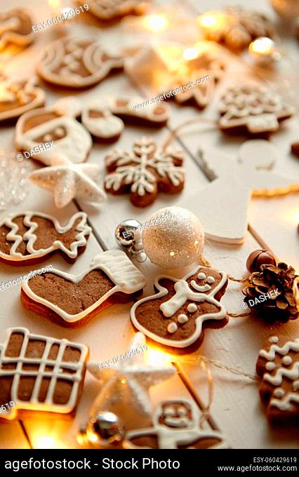 Christmas sweets composition. Gingerbread various shaped cookies with xmas decorations arranged on white wooden table with lights