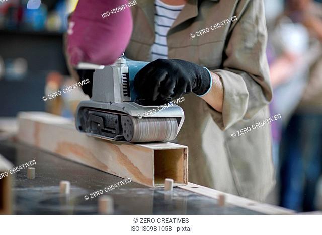 Cropped shot of female carpenter sanding wood in furniture making workshop