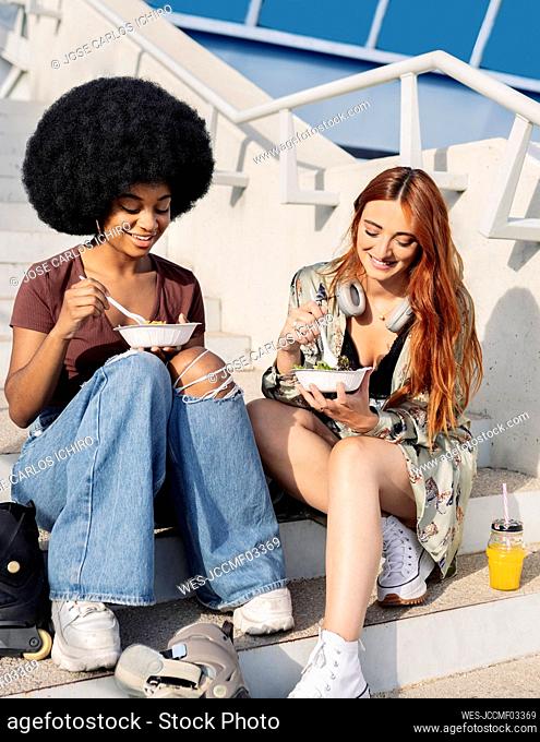 Smiling young female friends eating while sitting on steps