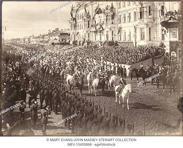 Tsar Nicolas II on horseback at the head of a procession in Russia, with soldiers and a large crowd, and people watching from two balconies