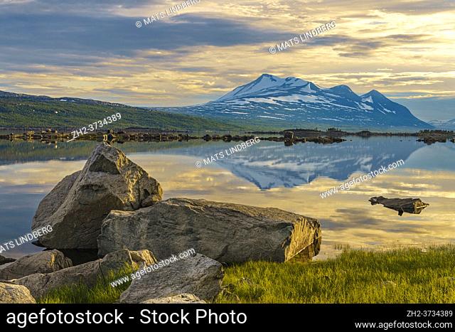 View over Mount Akka reflecting in the water, big rocks in the foreground, in nice evening light in the summer nigh, Stora sjöfallet nationalpark