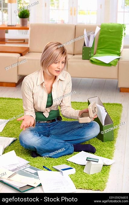Woman checking documents and credit card account, shocked by financial situation, sitting at home on floor