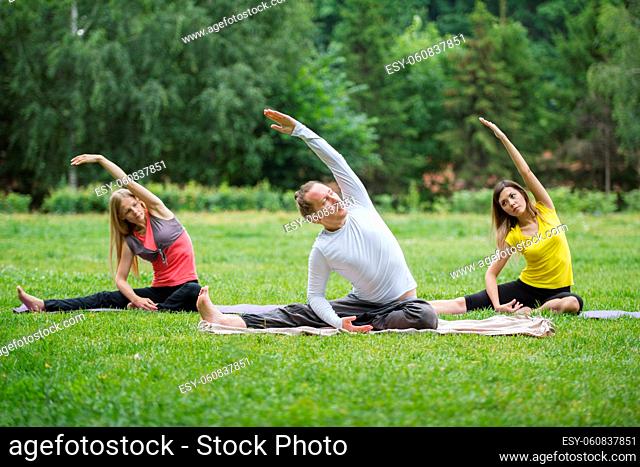 A group of yoga sportsmen performs breathing exercises in park, summer