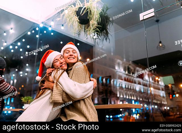Portrait of happy cute young friends hugging each other and smiling at caffe