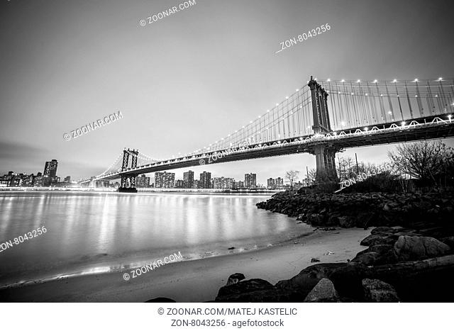 Manhattan bridge and New York City downtown skyline at dusk with skyscrapers illuminated over East River panorama. Copy space. Black and white image