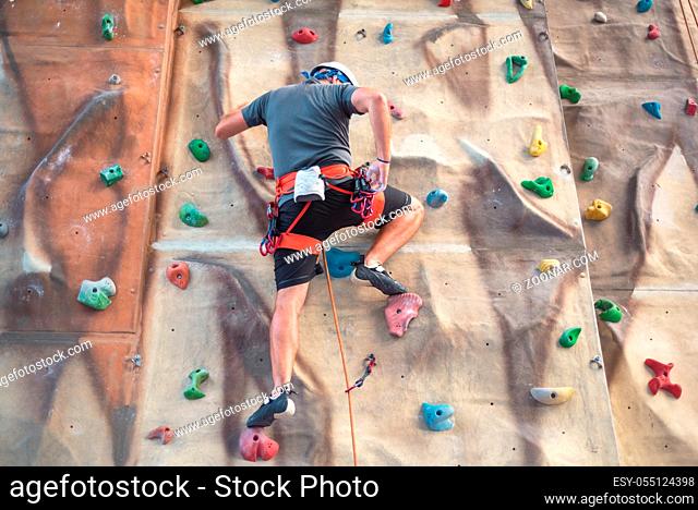Young man practicing rock climbing on artificial wall indoors