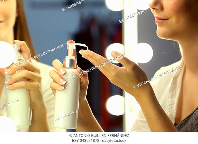 Portrait of a woman applying moisturizer cream on hands in front of a make up mirror