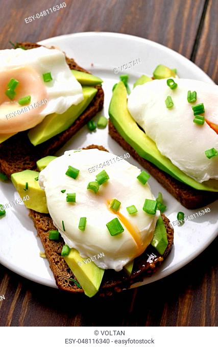 Tasty sandwiches with poached eggs and avocado over wooden background