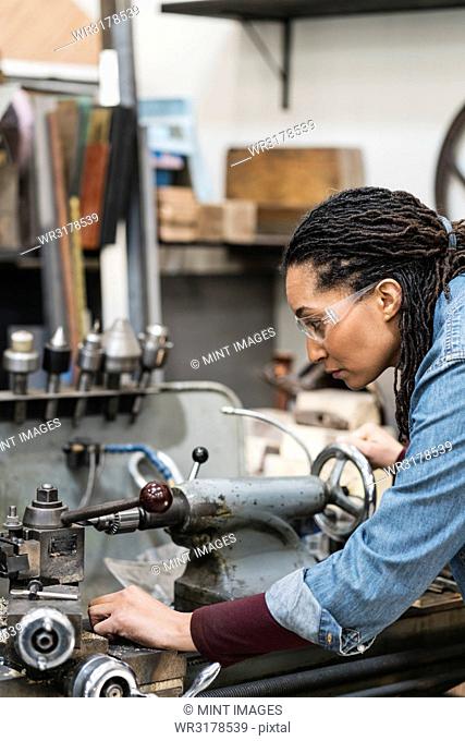 Woman wearing safety glasses standing in a metal workshop, working at a machine