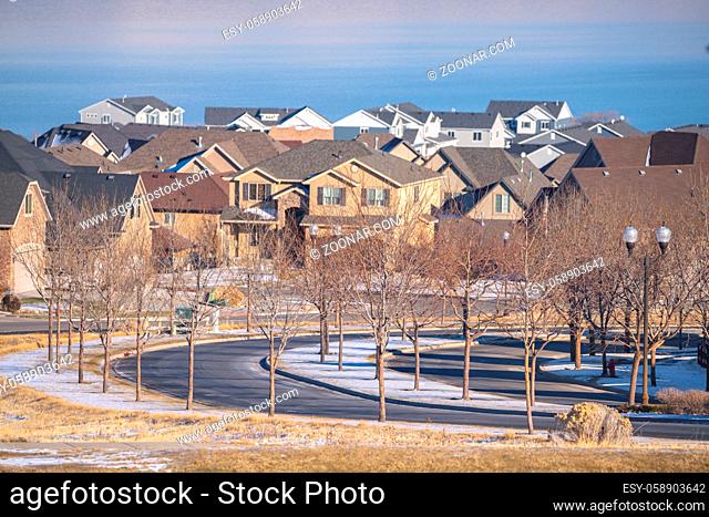 Curving bend in a tree lined street in winter with snow on the ground and view to a housing estate in Utah Valley