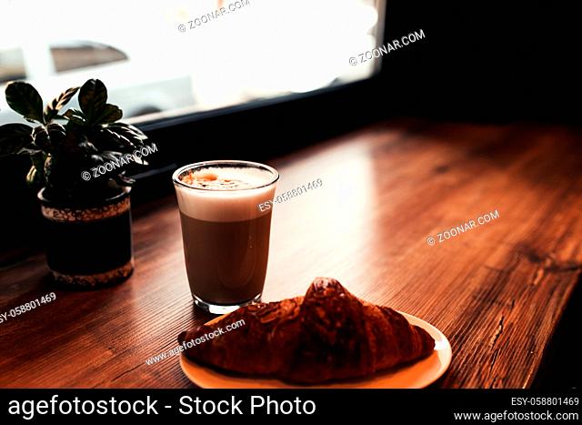 Cup of coffee, croissant at table near the window in cafe. Blurred background. High quality photo