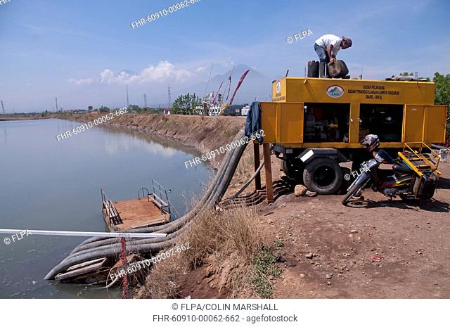 Worker on levee using water pump to drain mud lake of mud volcano, environmental disaster which developed after drilling incident, Porong Sidoarjo