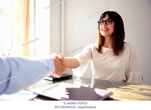 Happy Young Businesswoman Shaking Hand With Her Colleague Over Desk