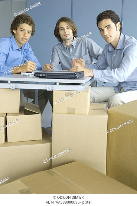 Businessmen sitting at table top supported by cardboard boxes, portrait