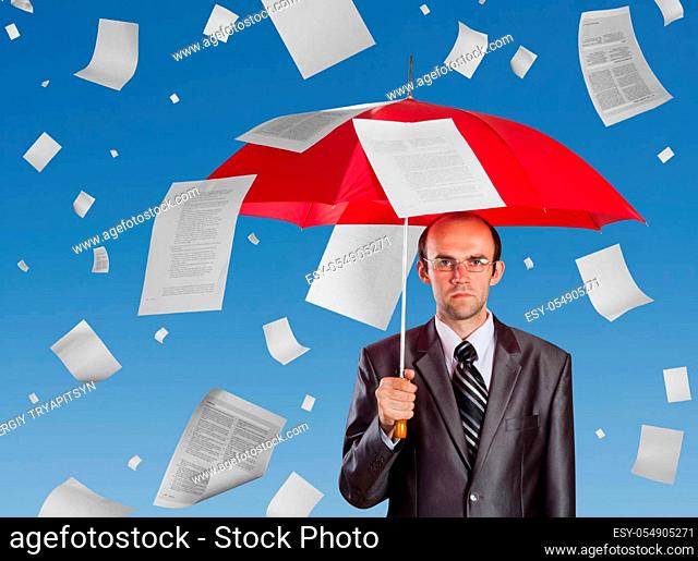 Serious businessman with red umbrella under falling documents