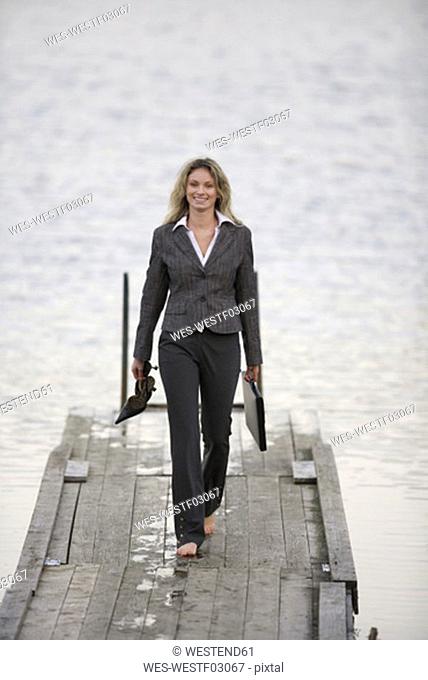 Businesswoman walking on jetty, holding shoes in hand