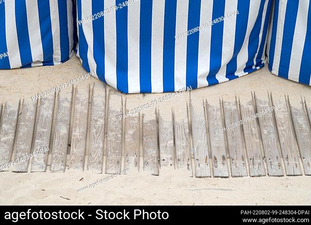 PRODUCTION - 29 July 2022, Portugal, Marinha Grande: A wooden walkway leads past blue and white striped beach cabins on the beach ""Sao Pedro de Moel""