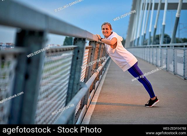 Smiling woman exercising near railing at bridge