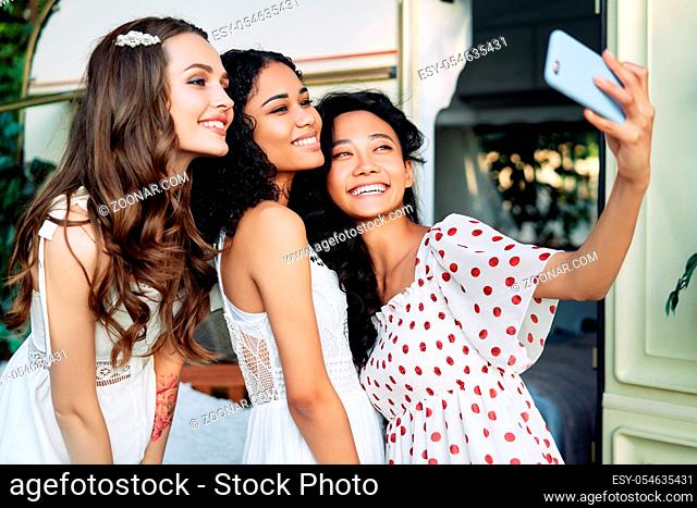 Beautiful smiling women taking selfie with mobile phone. Multi ethnic girls caucasian, african american and asian females making self portrait during picnic...