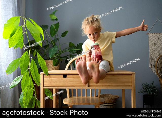 Girl gesturing thumbs up drinking smoothie at home