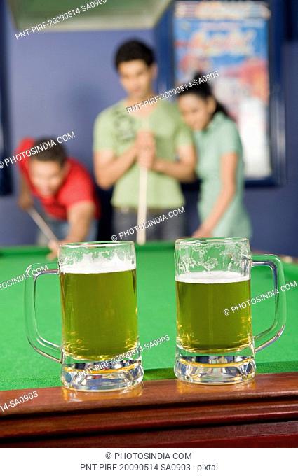 Beer glasses on a pool table with three friends playing in the background
