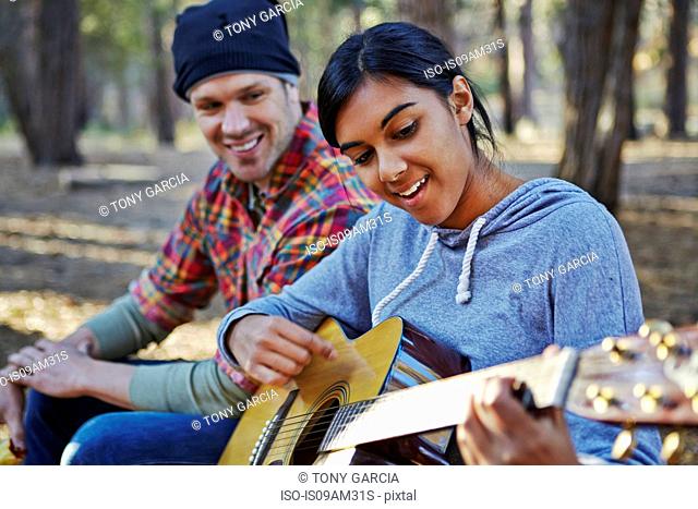 Young couple in forest playing acoustic guitar, Los Angeles, California, USA