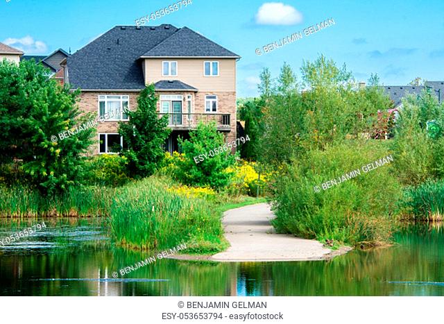 A large beautiful house stands on the shore of a small lake surrounded by trees and bushes