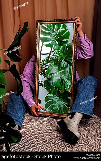 Jungles in the mirror. Woman holds mirror reflecting home jungles with Monstera plant