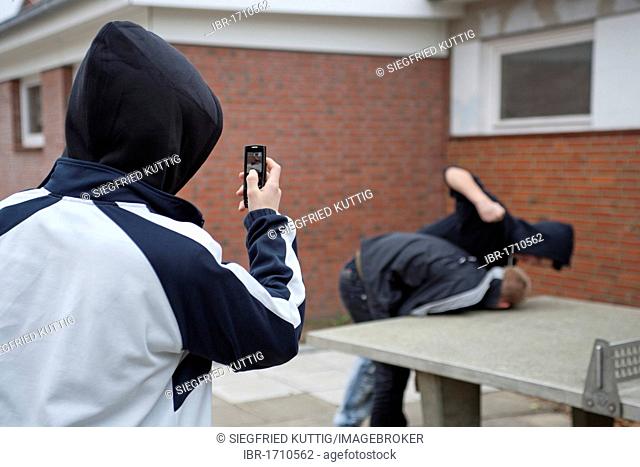 Boy being beaten on the playground while a third films with his cell phone, posed scene