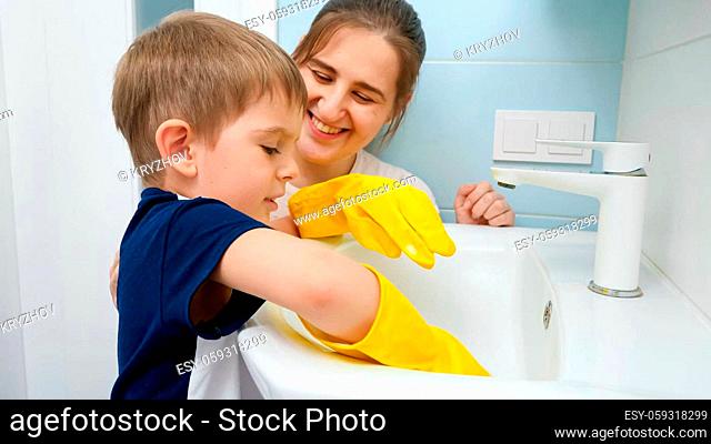 Smiling young mother looking at her little son helping with washing and cleaning house. Child doing housework and and helping parents