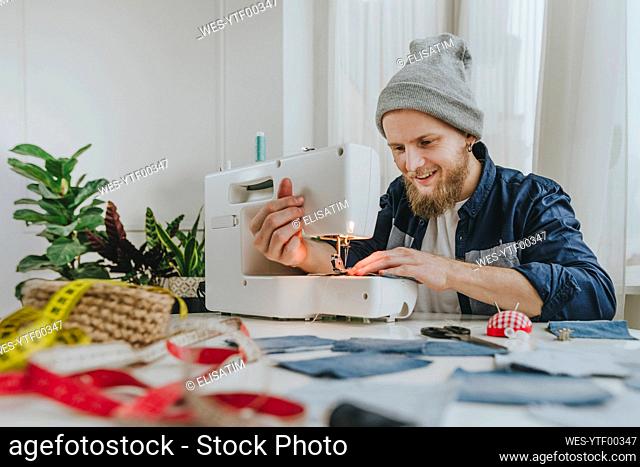 Smiling fashion designer working on sewing machine in workshop