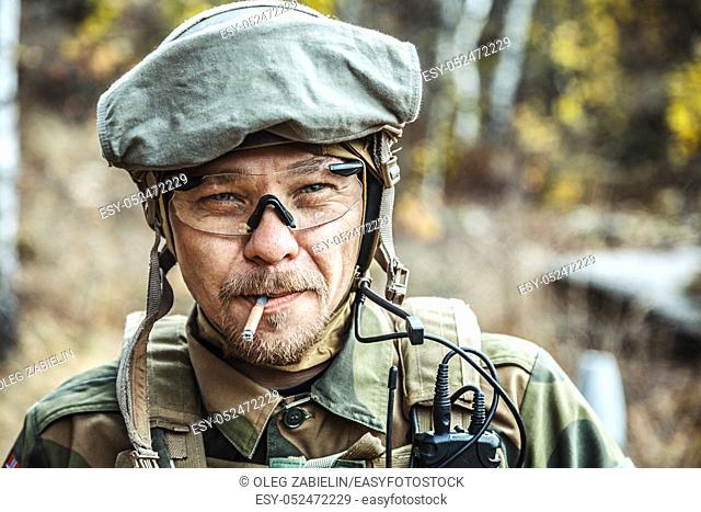 Norwegian Armed Forces Special Command FSK soldier smoking cigarette closeup portrait. Radio and headset are on