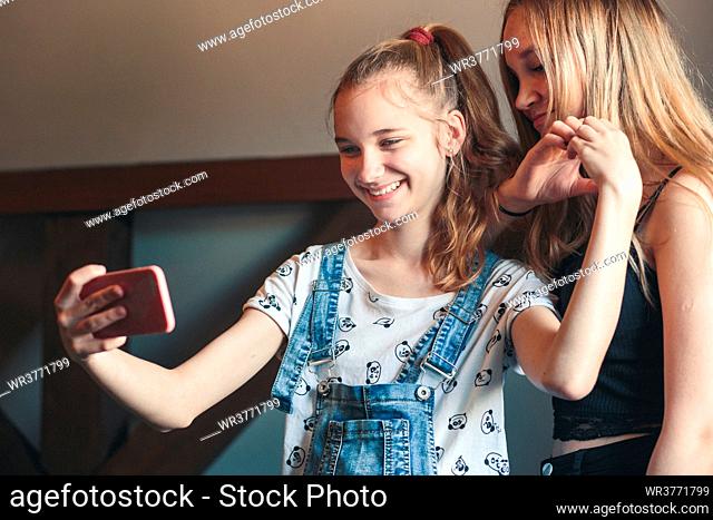 Young women taking selfie, using smartphone camera. Girls making faces, enjoying taking funny pictures together