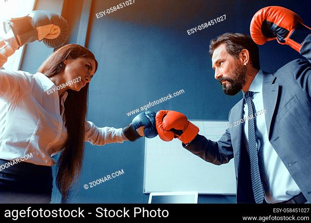 Handsome man and beautiful woman in office. Wearing boxing gloves. Compete in project. Fight of genders